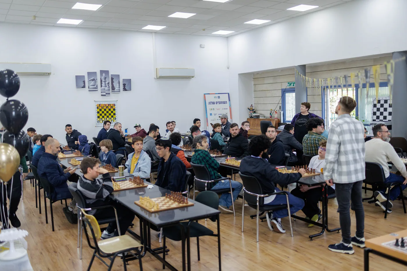 אולם האירוע מלא במשתתפים סביב לוחות השחמט